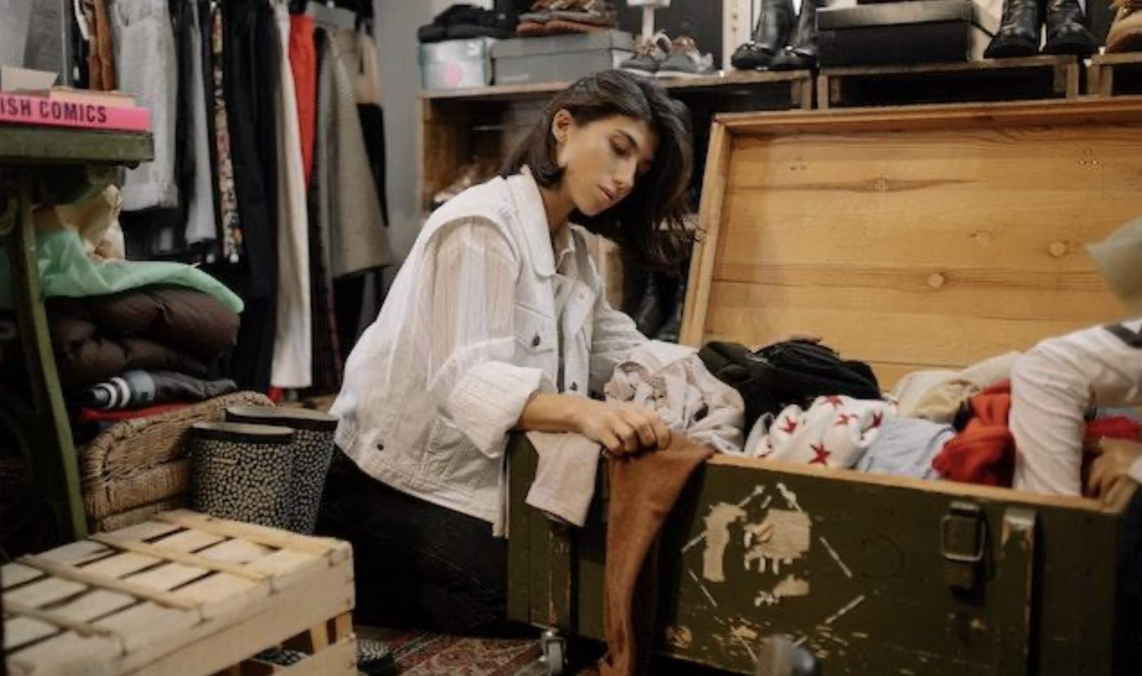 A woman sitting on the floor of a vintage wardrobe beside a wooden box